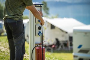 Attaching Camper RV Power Cable to Camping Electric Post During Camping Stay Motorhome RV Owner Attaching Power Cable to Camping Electric Post During Camping Stay
